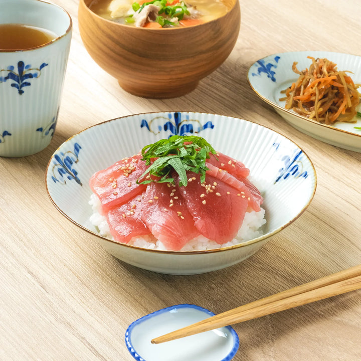 A ridged porcelain Japanese pasta bowl with blue floral leaf patterns, holding tuna sashimi on rice.