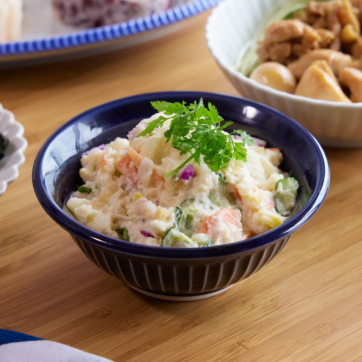 Japanese potato salad served in a deep blue Ginpo Kikka Lapis ceramic bowl, garnished with fresh herbs.