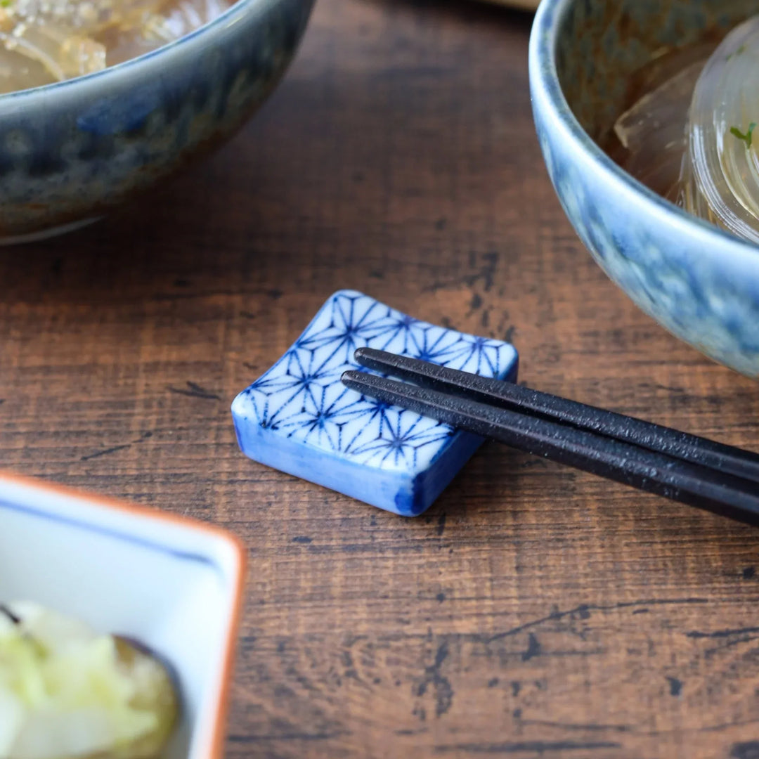 Square ceramic chopstick rest featuring a traditional Japanese hemp leaf pattern in blue, adding an elegant accent to a thoughtfully arranged table setting.