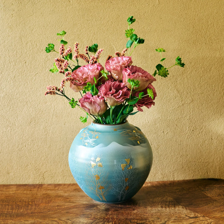 Hand-painted turquoise round vase with gold leaf motifs showcasing a lush bouquet of ruffled pink blooms and green foliage.