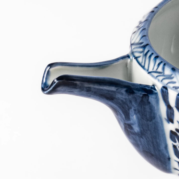 Porcelain sake pourer with spout featuring hand-painted indigo landscape and arabesque patterns in a traditional Japanese style.