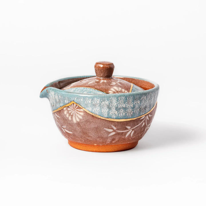 Ceramic teapot with lid featuring a turquoise crackle glaze and floral patterns in soft brown tones accented by a curved gold line.