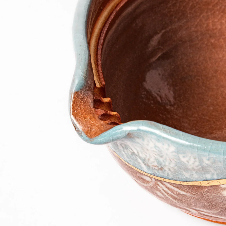 Ceramic teapot with lid featuring a turquoise crackle glaze and floral patterns in soft brown tones accented by a curved gold line.