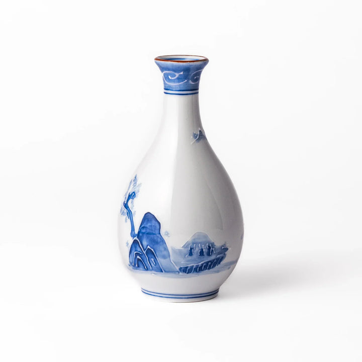 Porcelain sake flask with hand-painted blue mountain and village scenery, featuring a red rim and elegant traditional silhouette.