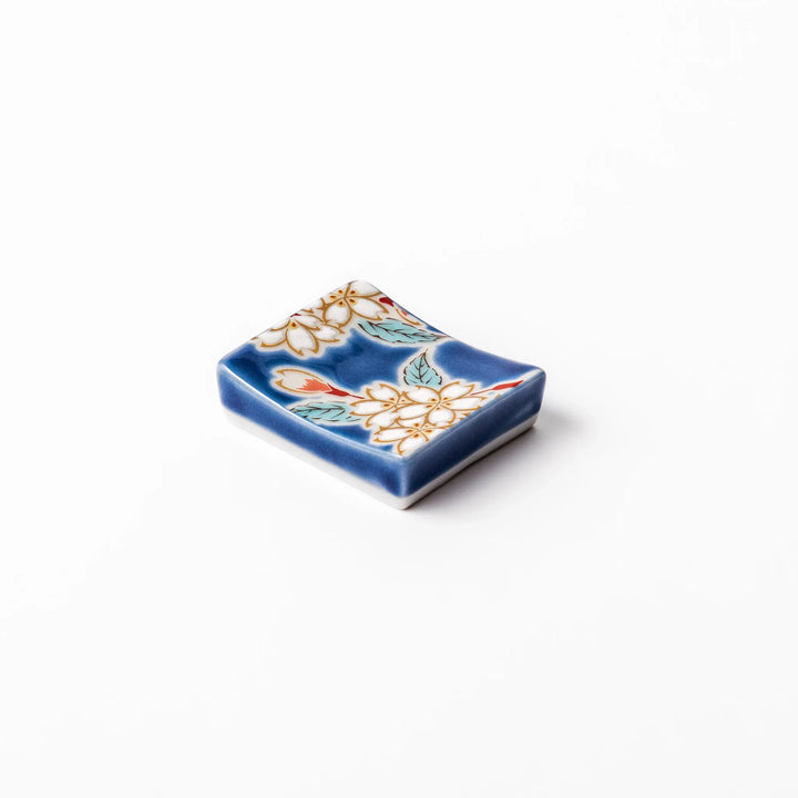 Rectangular blue Japanese ceramic chopstick rest with delicate white sakura blossoms and green leaves, ideal for traditional dining.