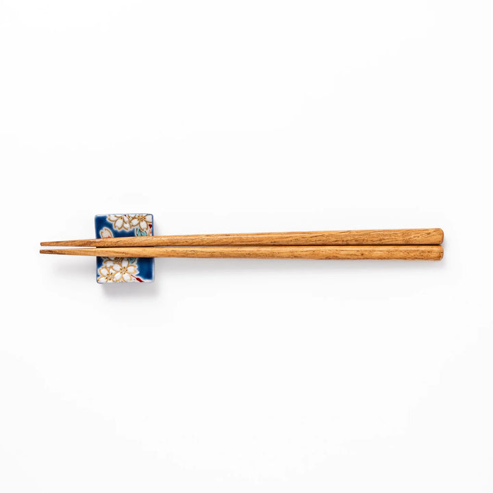 Rectangular blue Japanese ceramic chopstick rest with delicate white sakura blossoms and green leaves, ideal for traditional dining.