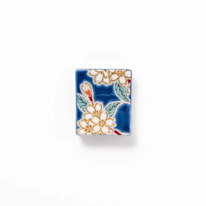 Rectangular blue Japanese ceramic chopstick rest with delicate white sakura blossoms and green leaves, ideal for traditional dining.