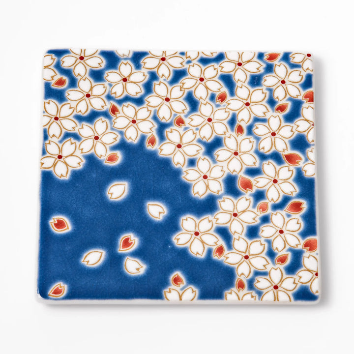 Square blue Japanese ceramic coaster with delicate white sakura blossoms and scattered petals, perfect for traditional dining settings.