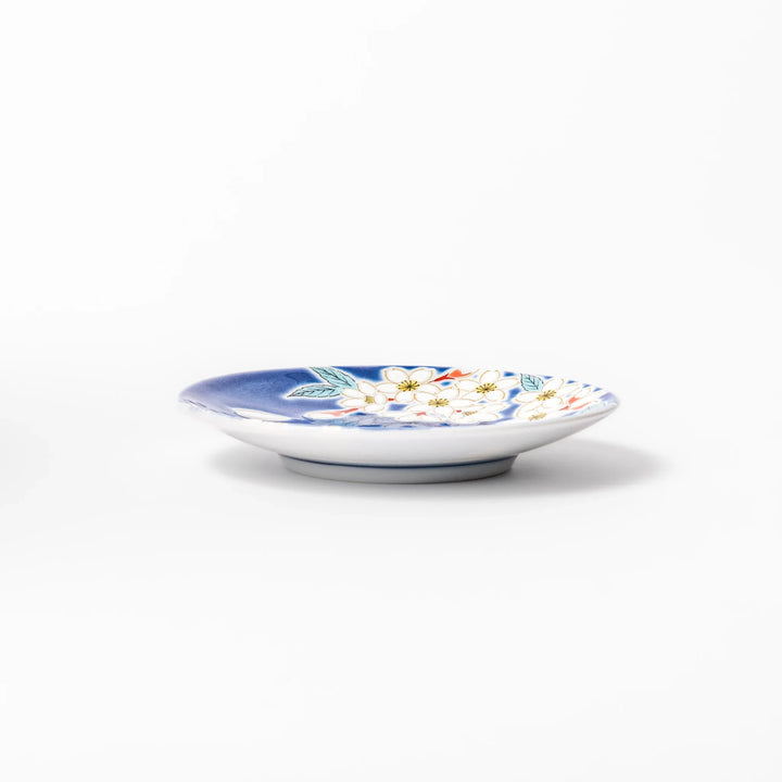 Blue Japanese ceramic sauce dish adorned with white sakura blossom and petals, ideal for traditional dining and serving soy sauce or condiments.