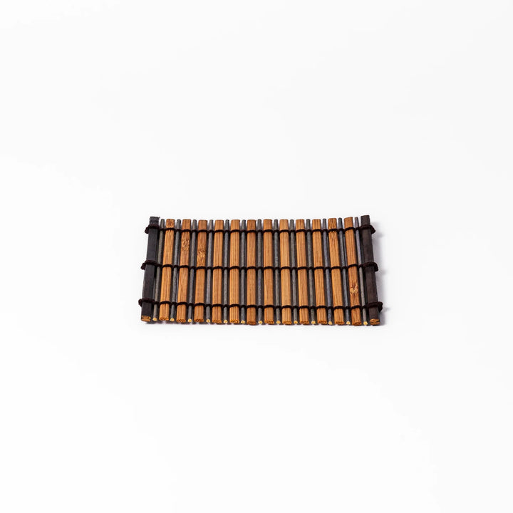 Brown bamboo coaster with alternating natural and dark slats, bound with black cord, adding a rustic and refined touch to Japanese-style tableware.