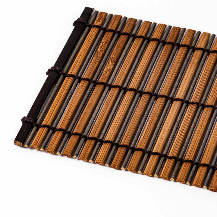 Brown bamboo coaster with alternating natural and dark slats, bound with black cord, adding a rustic and refined touch to Japanese-style tableware.