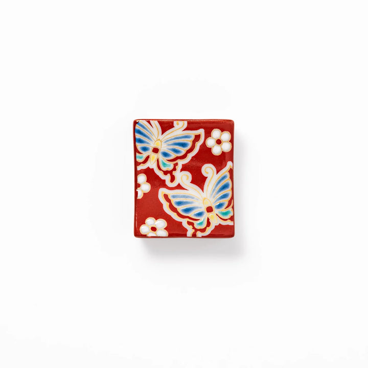 Japanese ceramic chopstick rest decorated with colorful butterflies and white blossoms on a vivid red background, adding charm to traditional table settings.