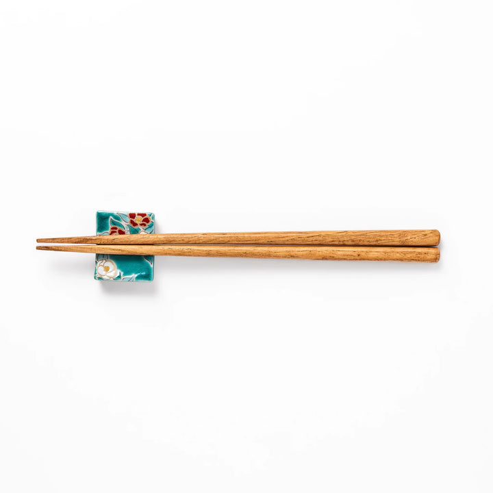 Japanese ceramic chopstick rest featuring red and white camellia blossom design on a glossy teal background, perfect for enhancing elegant table settings.