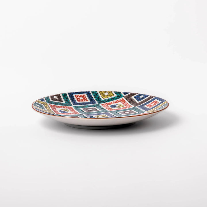 Colorful porcelain dessert plate featuring a mosaic of geometric square patterns in red, green, yellow, blue, and black with floral accents.
