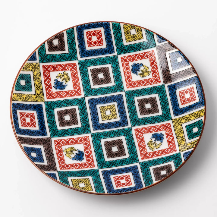 Colorful porcelain dessert plate featuring a mosaic of geometric square patterns in red, green, yellow, blue, and black with floral accents.