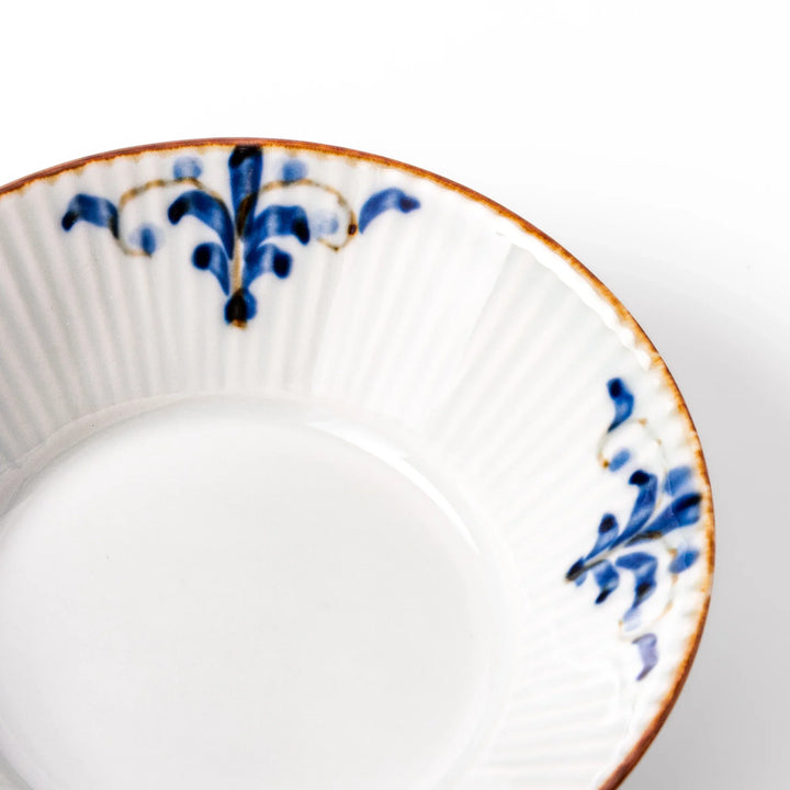White dessert bowl with vertical ridges, blue floral accents around the rim, and a warm brown edge, perfect for sweets or fruit.