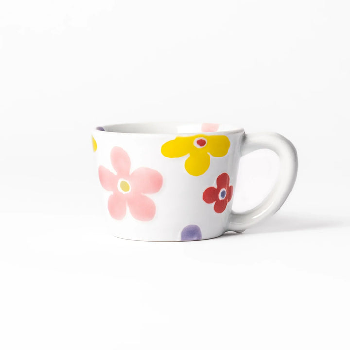 White ceramic kids mug with pink, yellow, red, and purple flower motifs, round handle, shown held for scale