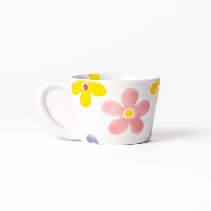 White ceramic kids mug with pink, yellow, red, and purple flower motifs, round handle, shown held for scale