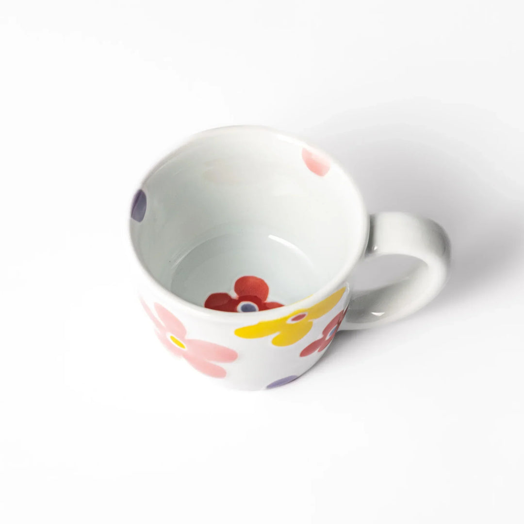 White ceramic kids mug with pink, yellow, red, and purple flower motifs, round handle, shown held for scale