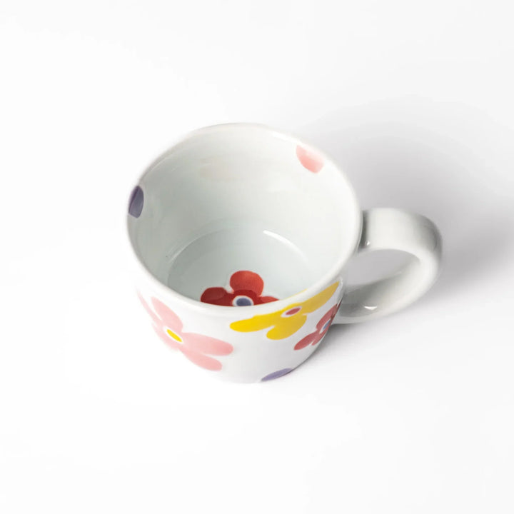 White ceramic kids mug with pink, yellow, red, and purple flower motifs, round handle, shown held for scale