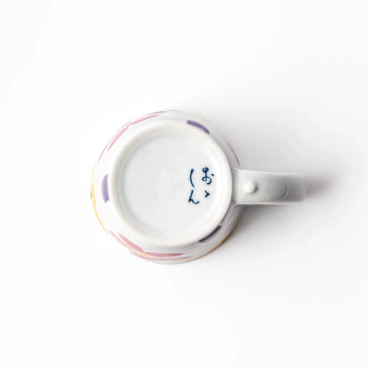 White ceramic kids mug with pink, yellow, red, and purple flower motifs, round handle, shown held for scale