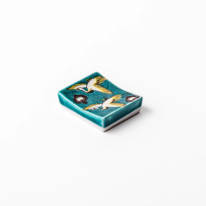 Rectangular Japanese ceramic chopstick rest featuring flying crane motif with teal geometric background and gold accents, symbolizing longevity and elegance in dining.