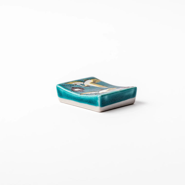 Rectangular Japanese ceramic chopstick rest featuring flying crane motif with teal geometric background and gold accents, symbolizing longevity and elegance in dining.