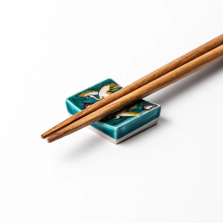 Rectangular Japanese ceramic chopstick rest featuring flying crane motif with teal geometric background and gold accents, symbolizing longevity and elegance in dining.