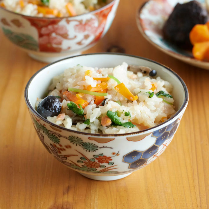 Japanese porcelain rice bowl with floral and geometric patterns, filled with colorful mixed rice with carrots, greens, and mushrooms.
