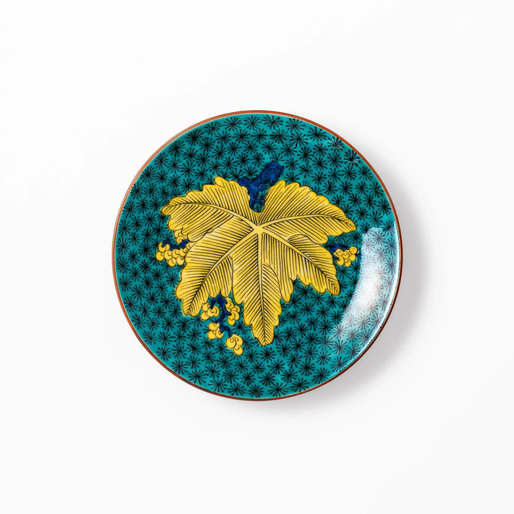 Round Kutani dessert plate with a bold golden leaf and grape motif on a turquoise background patterned with black starbursts.