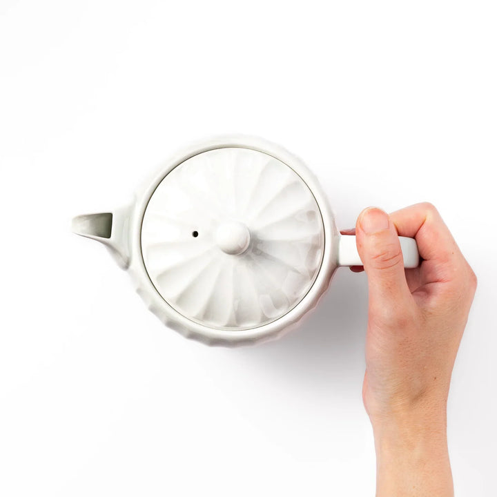 White teapot with vertical petal-inspired ridges and a round lid, perfect for a refined and elegant tea presentation.