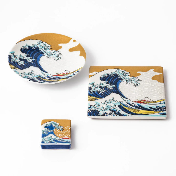 Japanese ceramic tableware set featuring Hokusai’s Great Wave design with vivid blue waves, golden sky, and Mt. Fuji, including sauce dish, coaster, and chopstick rest.