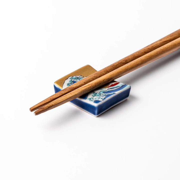 Rectangular Japanese ceramic chopstick rest featuring Hokusai’s Great Wave design with vivid blue wave, golden sky, and Mt. Fuji, adding iconic artistry to dining.