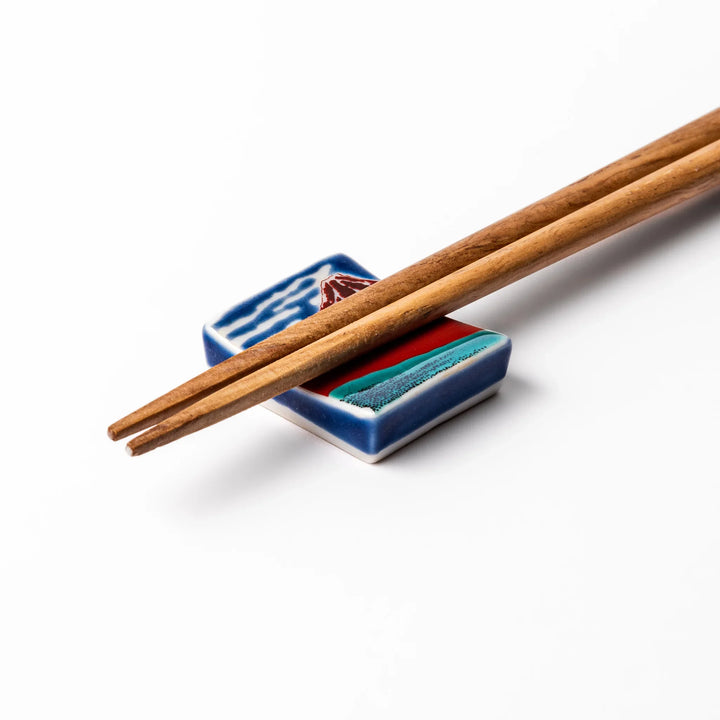 Rectangular Japanese ceramic chopstick rest featuring Hokusai’s Red Fuji design with vivid red mountain and blue sky, bringing iconic artistry to dining tables.