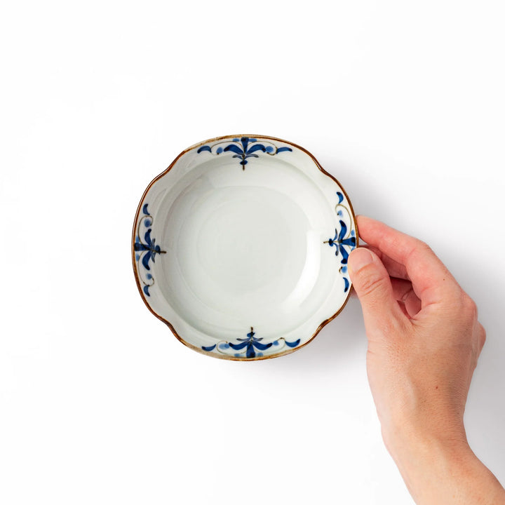 White ceramic cereal bowl with a scalloped rim, decorated inside with blue leaf motifs and a brown-accented edge.