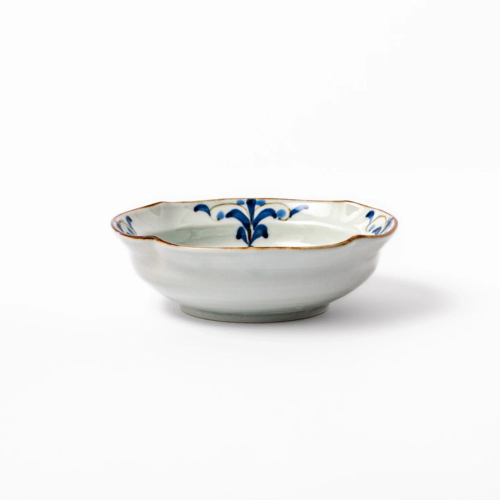 White ceramic cereal bowl with a scalloped rim, decorated inside with blue leaf motifs and a brown-accented edge.