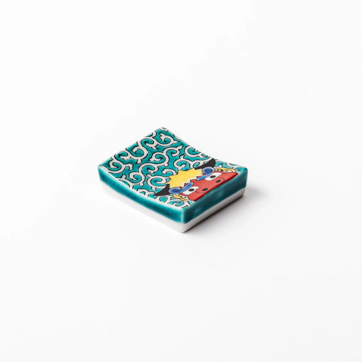 Rectangular Japanese ceramic chopstick rest featuring a bold red lion dance motif with green swirl background, adding festive tradition to dining tables.