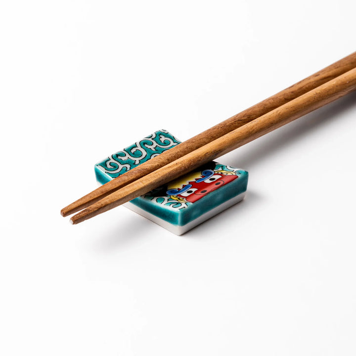 Rectangular Japanese ceramic chopstick rest featuring a bold red lion dance motif with green swirl background, adding festive tradition to dining tables.