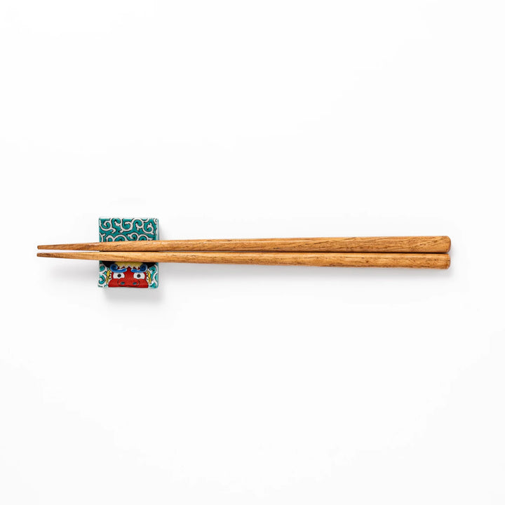 Rectangular Japanese ceramic chopstick rest featuring a bold red lion dance motif with green swirl background, adding festive tradition to dining tables.