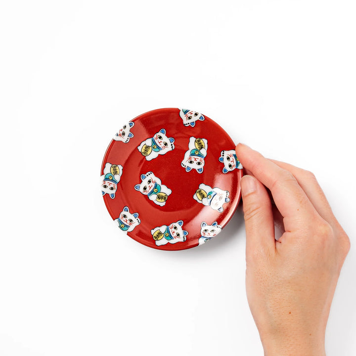 Round Japanese ceramic sauce dish with a red background decorated with playful maneki neko lucky cats, perfect for serving soy sauce or small condiments.