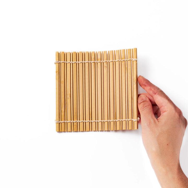 Natural finish bamboo coaster with uniform vertical slats and white cord ties, bringing a warm, organic accent to your Japanese-style table setting.