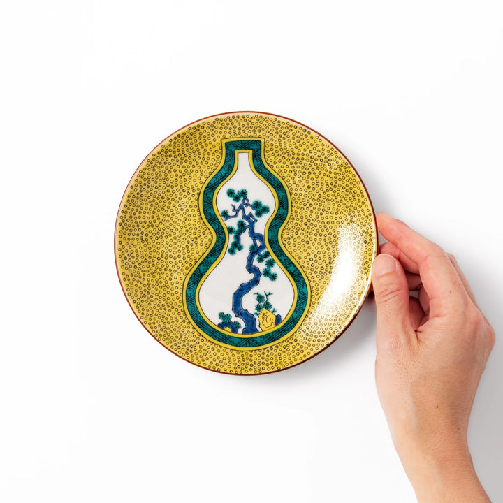 Japanese dessert plate featuring a yellow patterned background with a gourd-shaped center, showcasing a blue pine tree and green foliage.