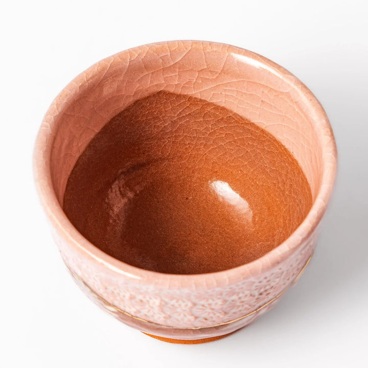 Ceramic tea cup with a crackled pink glaze, floral patterns, and a soft gold accent line blending traditional charm with handmade warmth.