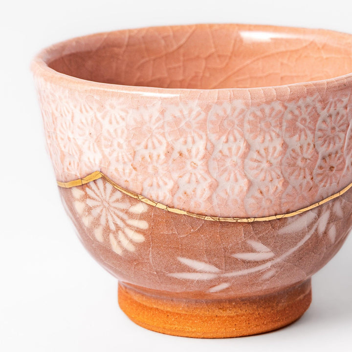 Ceramic tea cup with a crackled pink glaze, floral patterns, and a soft gold accent line blending traditional charm with handmade warmth.