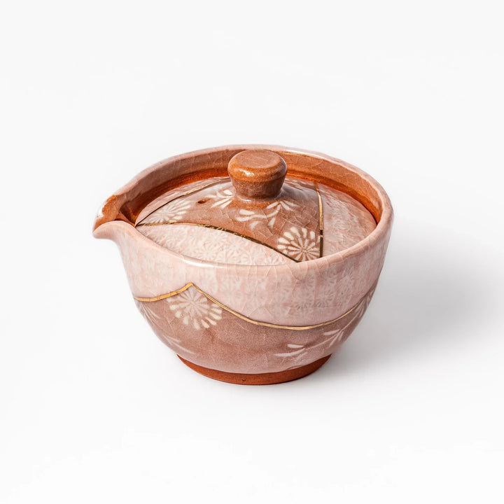 Ceramic teapot with a soft pink crackled glaze, floral patterns, and a curved spout accented by a hand-applied gold line for an artisanal touch.