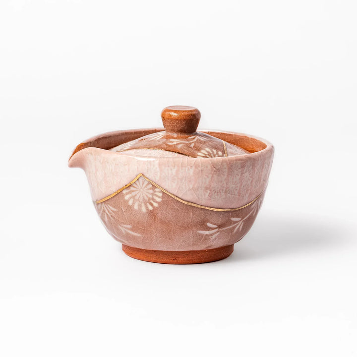 Ceramic teapot with a soft pink crackled glaze, floral patterns, and a curved spout accented by a hand-applied gold line for an artisanal touch.