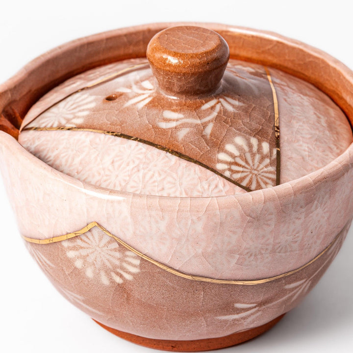 Ceramic teapot with a soft pink crackled glaze, floral patterns, and a curved spout accented by a hand-applied gold line for an artisanal touch.