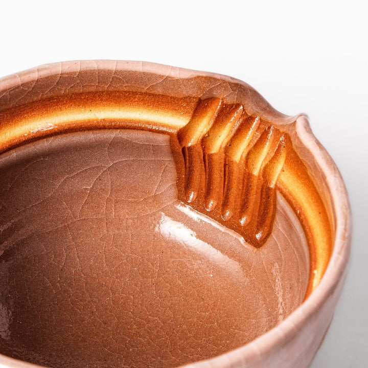 Ceramic teapot with a soft pink crackled glaze, floral patterns, and a curved spout accented by a hand-applied gold line for an artisanal touch.