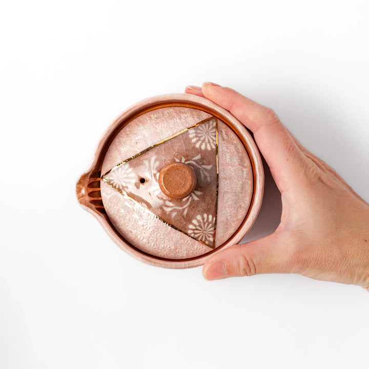 Ceramic teapot with a soft pink crackled glaze, floral patterns, and a curved spout accented by a hand-applied gold line for an artisanal touch.
