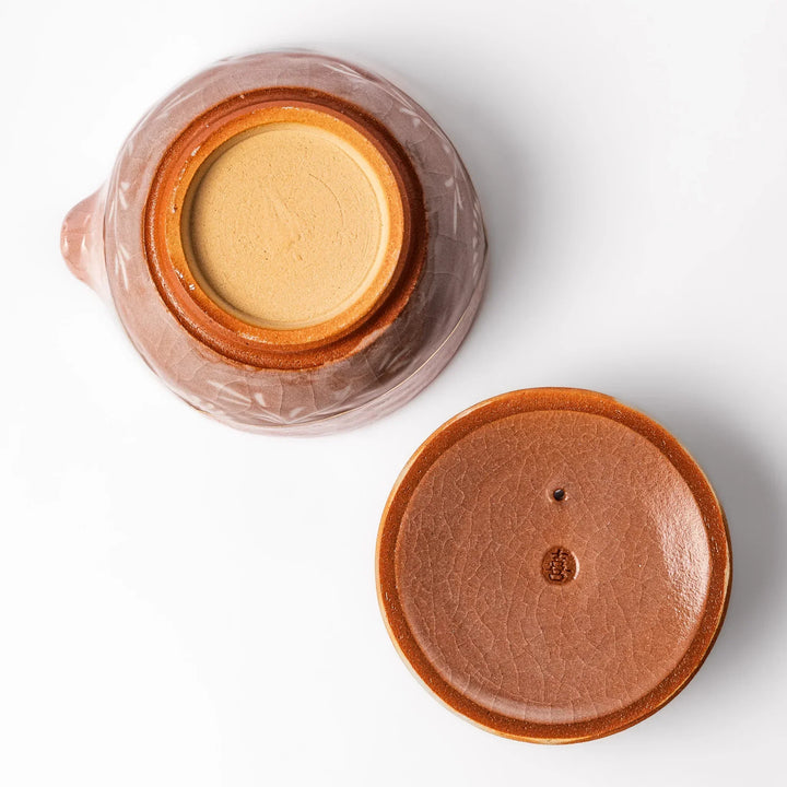 Ceramic teapot with a soft pink crackled glaze, floral patterns, and a curved spout accented by a hand-applied gold line for an artisanal touch.